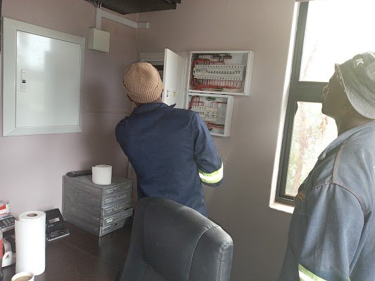 Two electricians installing and wiring new distribution boards inside an office